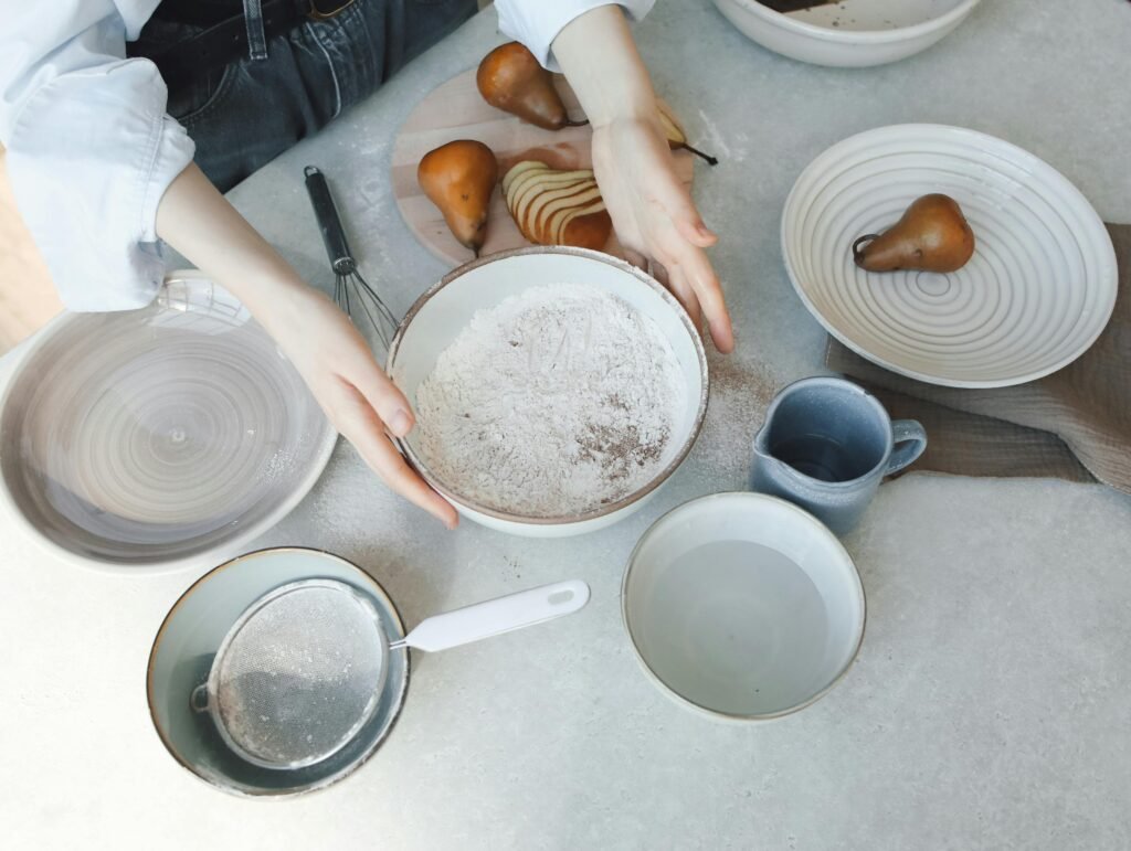 Top view of a person preparing ingredients for baking with fresh pears and flour.